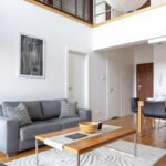 Two-floor apartment with stylish living room with grey sofa and wooden coffee table open to dining area with table for four